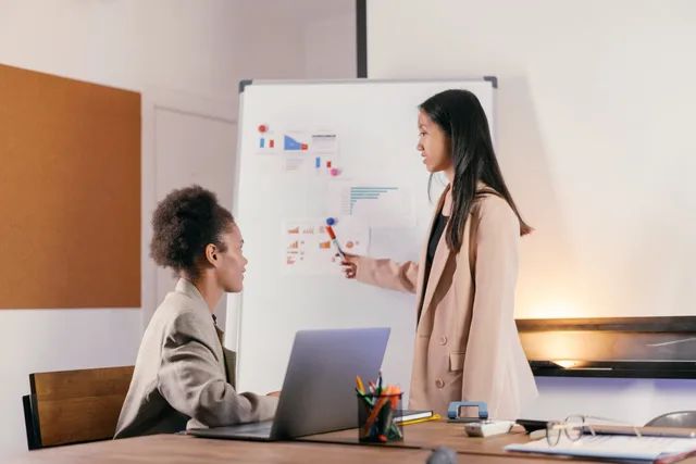 Two professionals engaged in a business meeting, discussing graphs on a whiteboard. A workflow for approving influencer rates