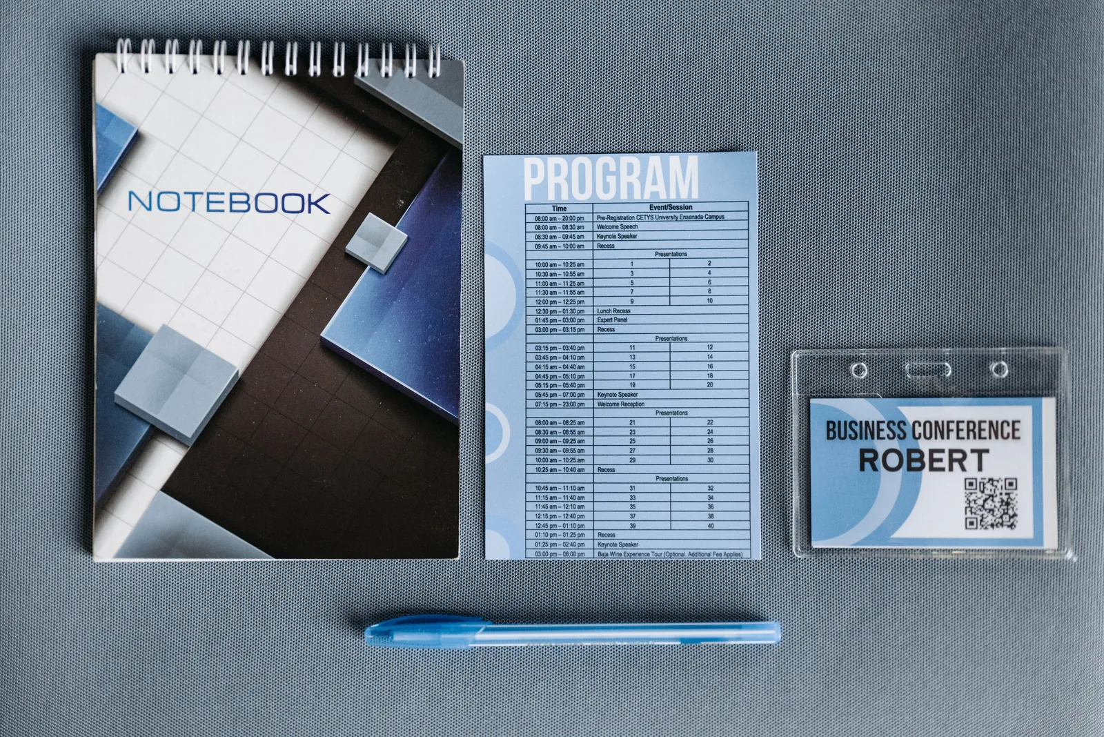 Flatlay of a notebook, conference badge, pen, and program on gray surface.