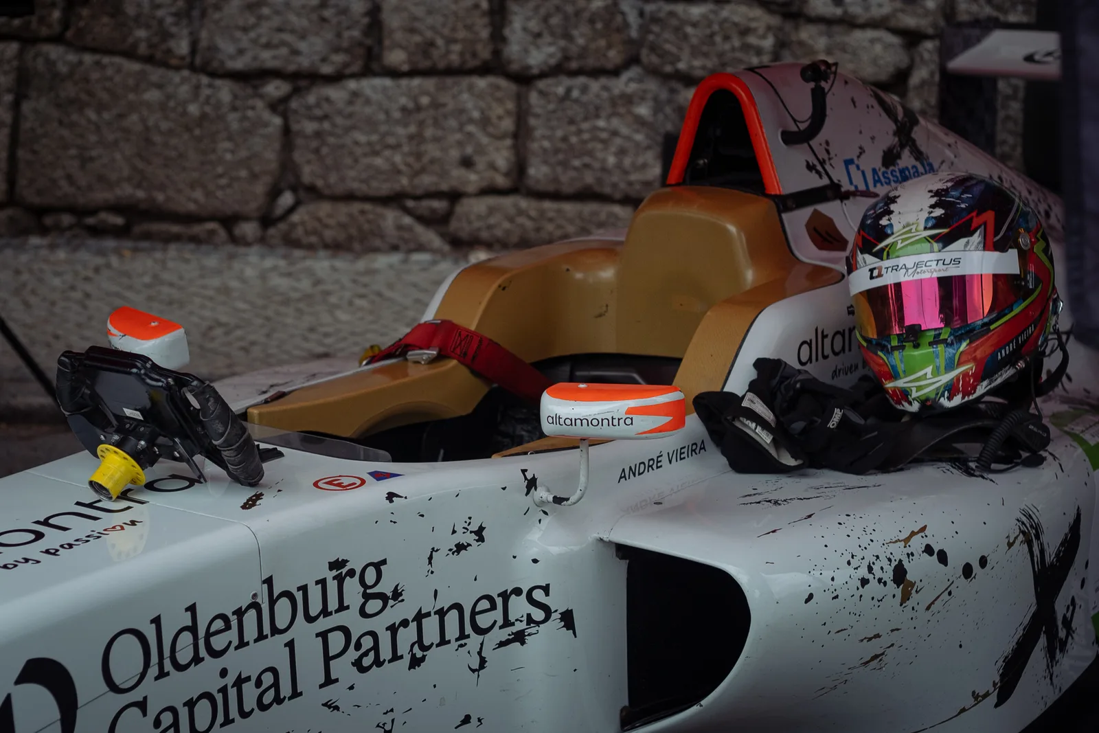 Close-up of a racing car's interior featuring a helmet and sponsorship branding.